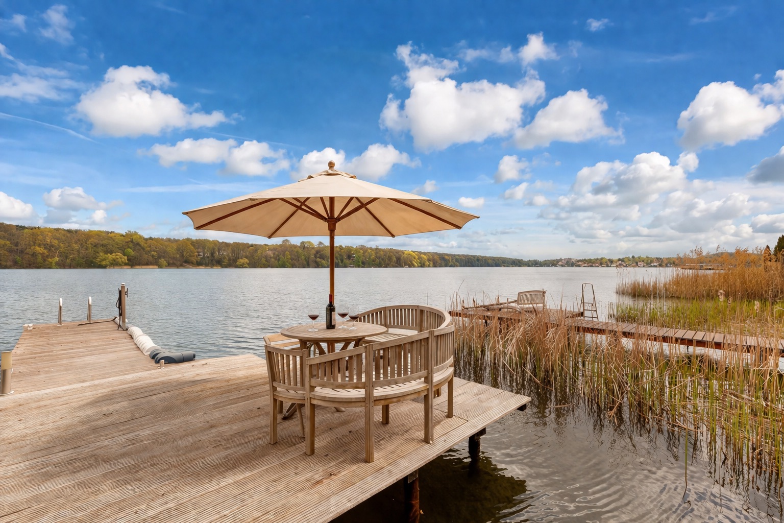 Holzterrasse am See mit Rundtisch, Stühlen und Sonnenschirm.