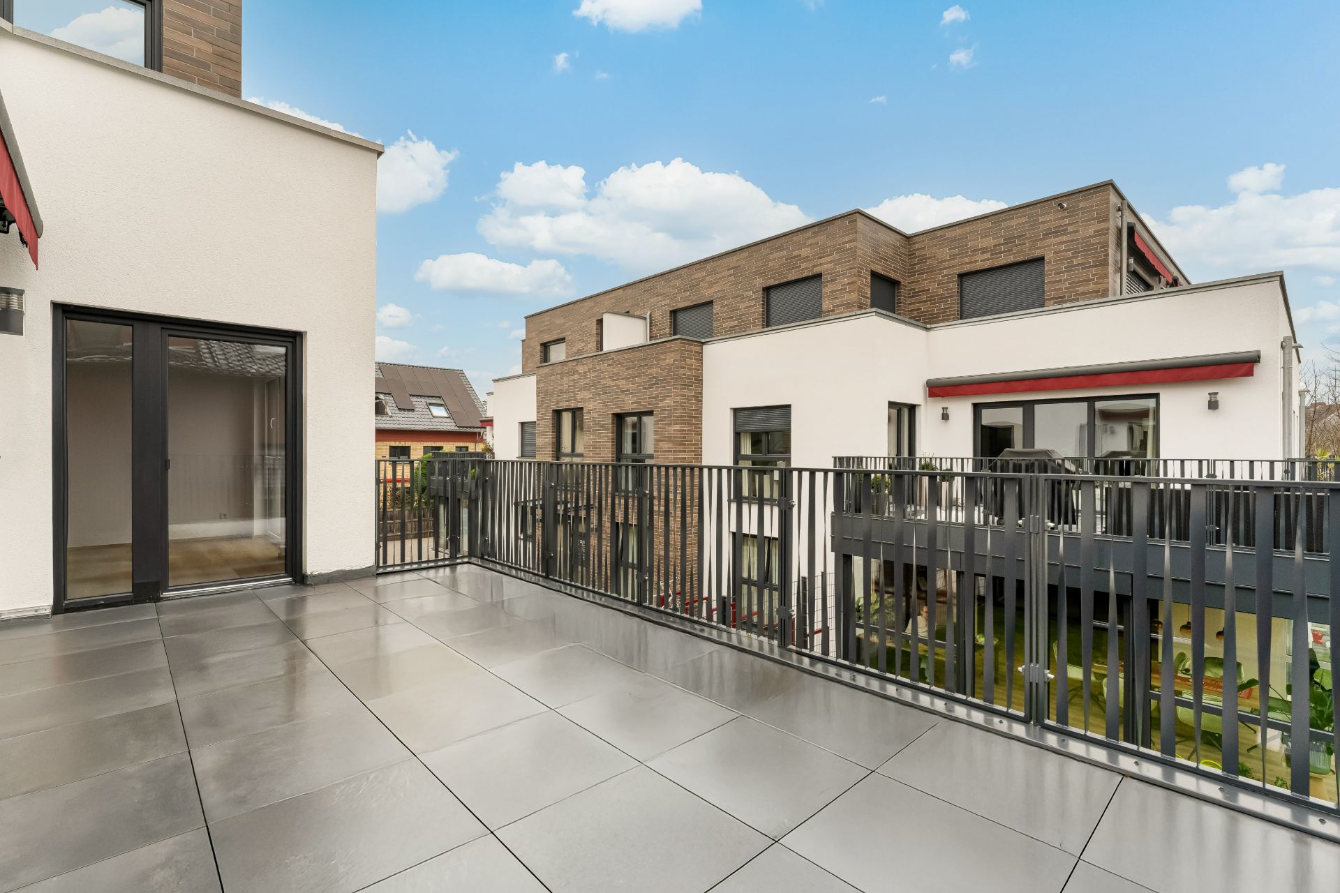 Große, moderne Dachterrasse mit Fliesenboden und Metallgeländer, Blick auf benachbarte Häuser.