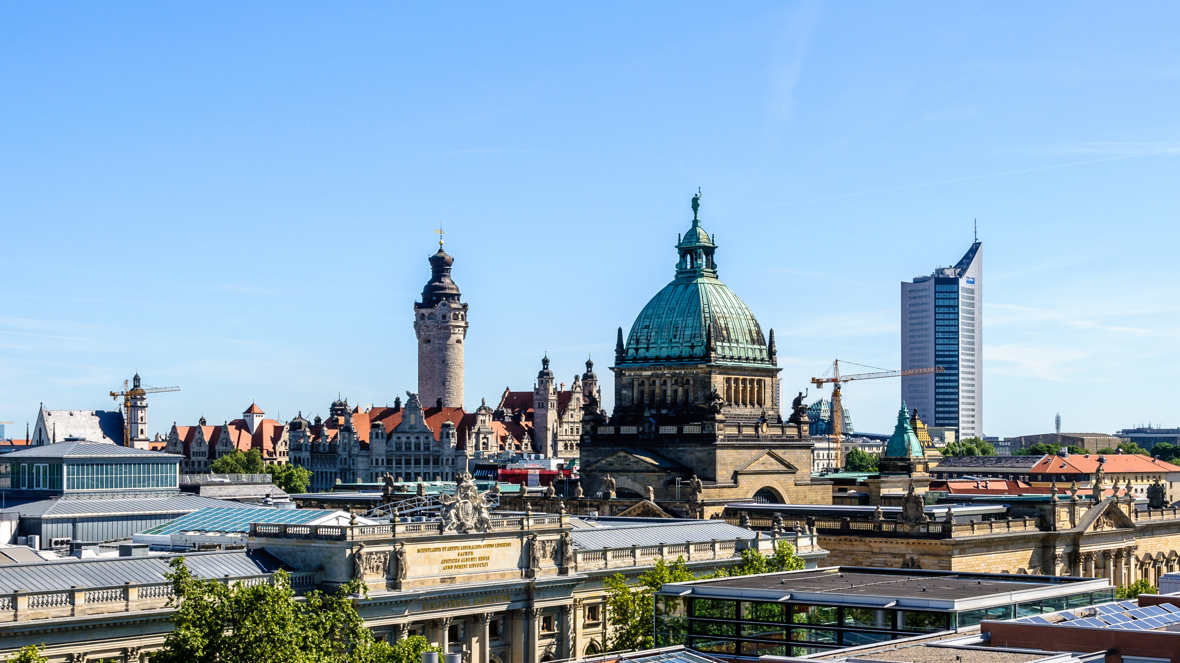 Stadtansicht mit historischen Gebäuden, Kuppel und modernem Hochhaus bei blauem Himmel.