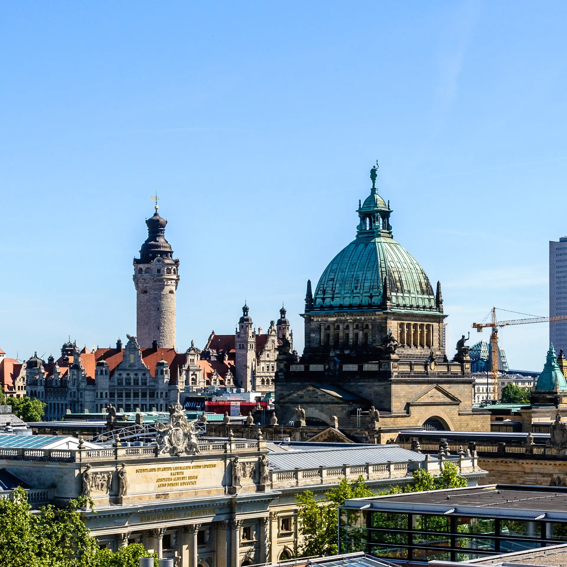 Stadtansicht mit historischen Gebäuden, Kuppel und modernem Hochhaus bei blauem Himmel.