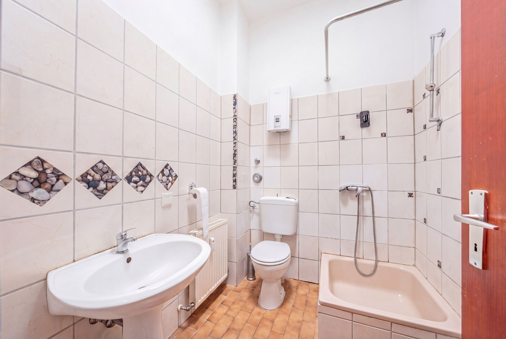 Helles Badezimmer mit Waschbecken, Toilette und beiger Dusche, gefliest mit Kieselstein-Motiven.