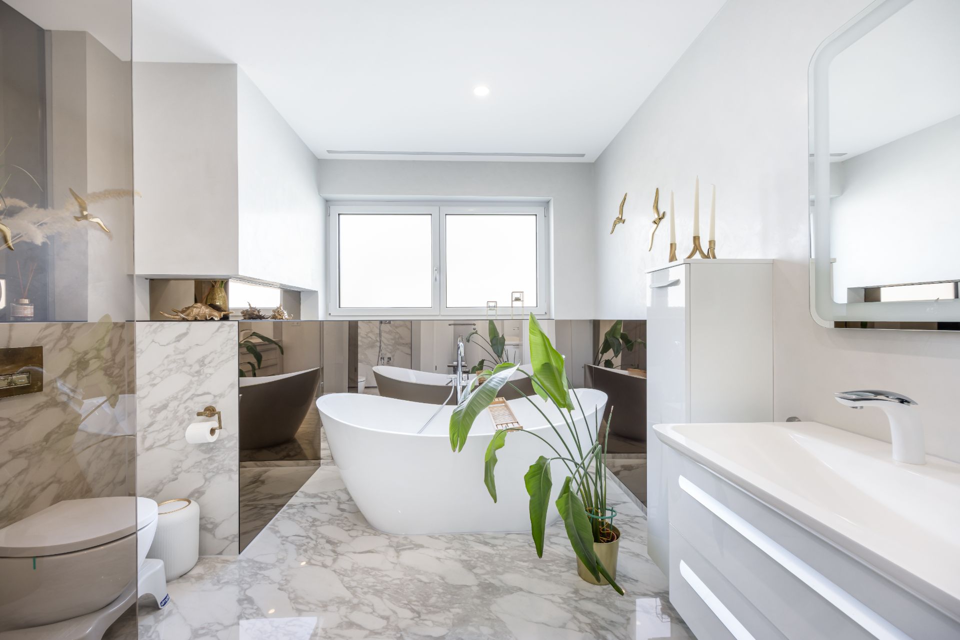 Modernes Badezimmer mit freistehender Badewanne, Pflanzen und großem Fenster.