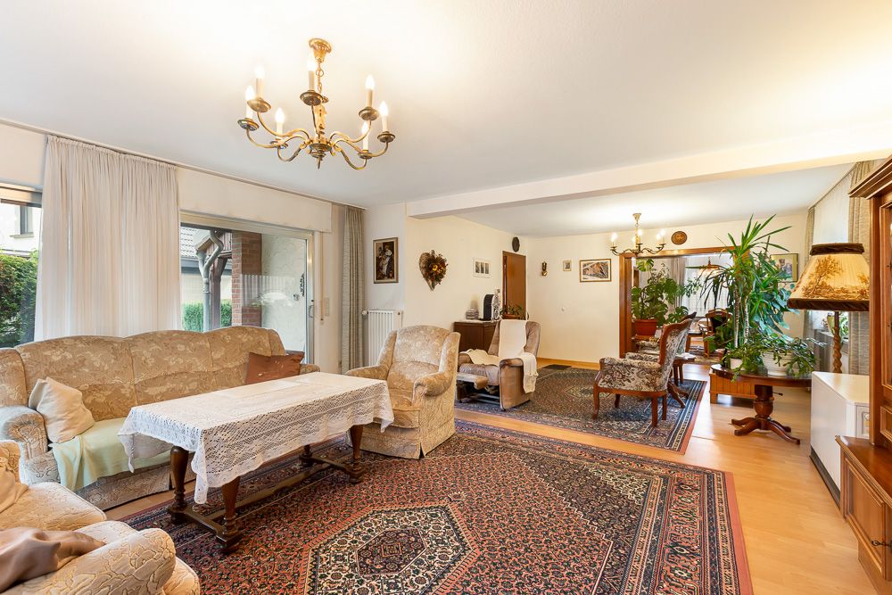 Helles Wohnzimmer mit gemustertem Teppich, Polstermöbeln, großem Fenster und Pflanzen.
