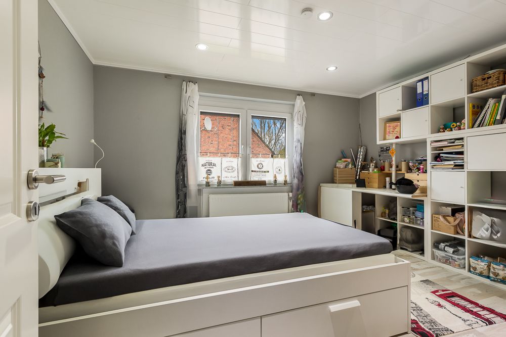 Modernes Schlafzimmer mit grauen Wänden, Doppelbett und Regalen mit Aufbewahrungsboxen an der rechten Wand.