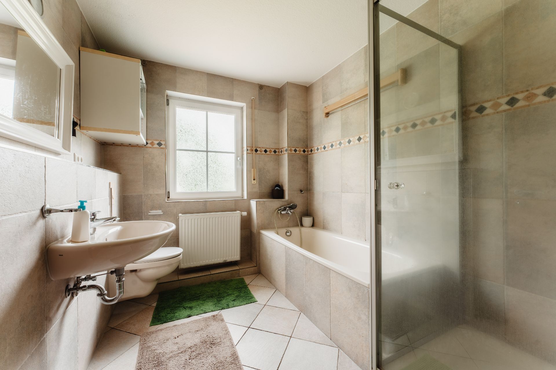 Helles Badezimmer mit Badewanne, Dusche, Waschbecken, Toilette und Fenster.