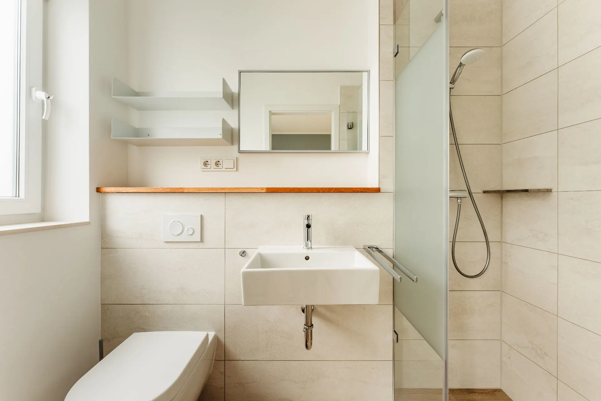 Modernes, helles Badezimmer mit Waschbecken, Toilette, Dusche und Regal über dem Waschbecken.