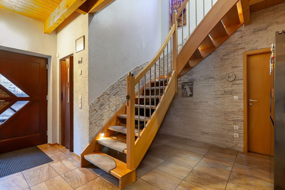 Heller Eingangsbereich mit Holztreppe, Fliesenboden und brauner Haustür.