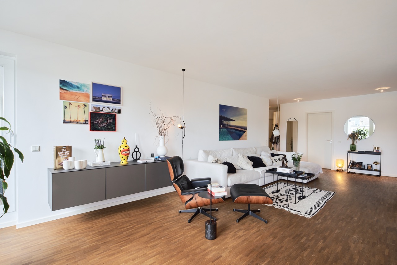 Modernes Wohnzimmer mit weißem Sofa, Sessel, Holzboden und dekorierten Wänden.