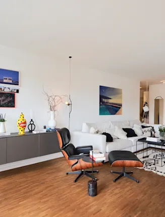 Modernes Wohnzimmer mit weißem Sofa, Sessel, Holzboden und dekorierten Wänden.