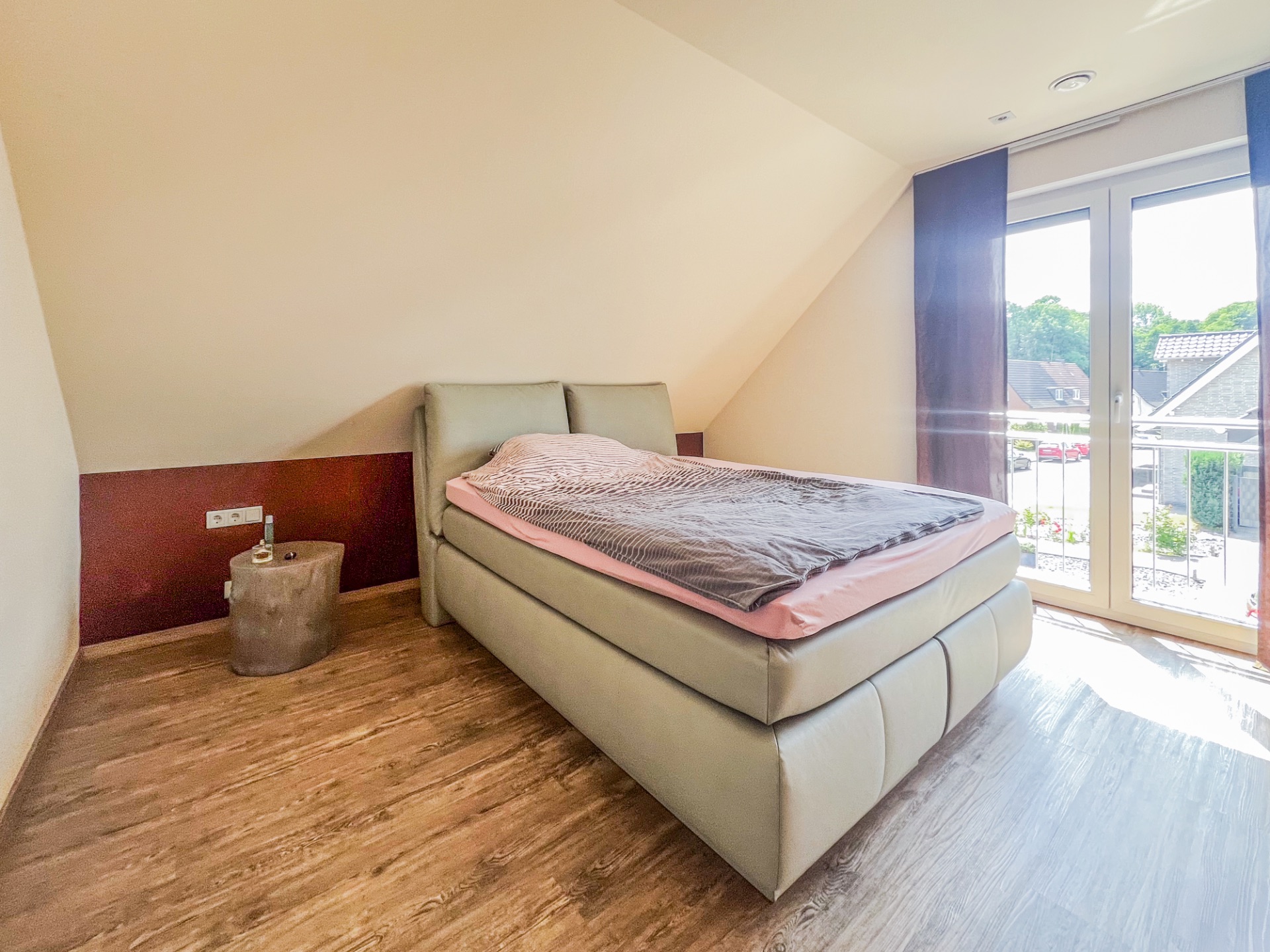 Helles Schlafzimmer mit Doppelbett, kleinem Nachttisch und Fenster mit Blick nach draußen.