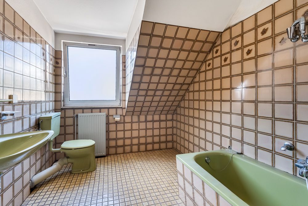 Badezimmer mit grüner Badewanne, grünem WC und grünem Waschbecken, beige Fliesen, Fenster.