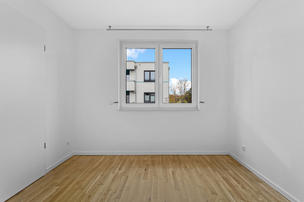 Leerer Raum mit Holzboden und Fenster, durch das man ein Nachbargebäude sieht.