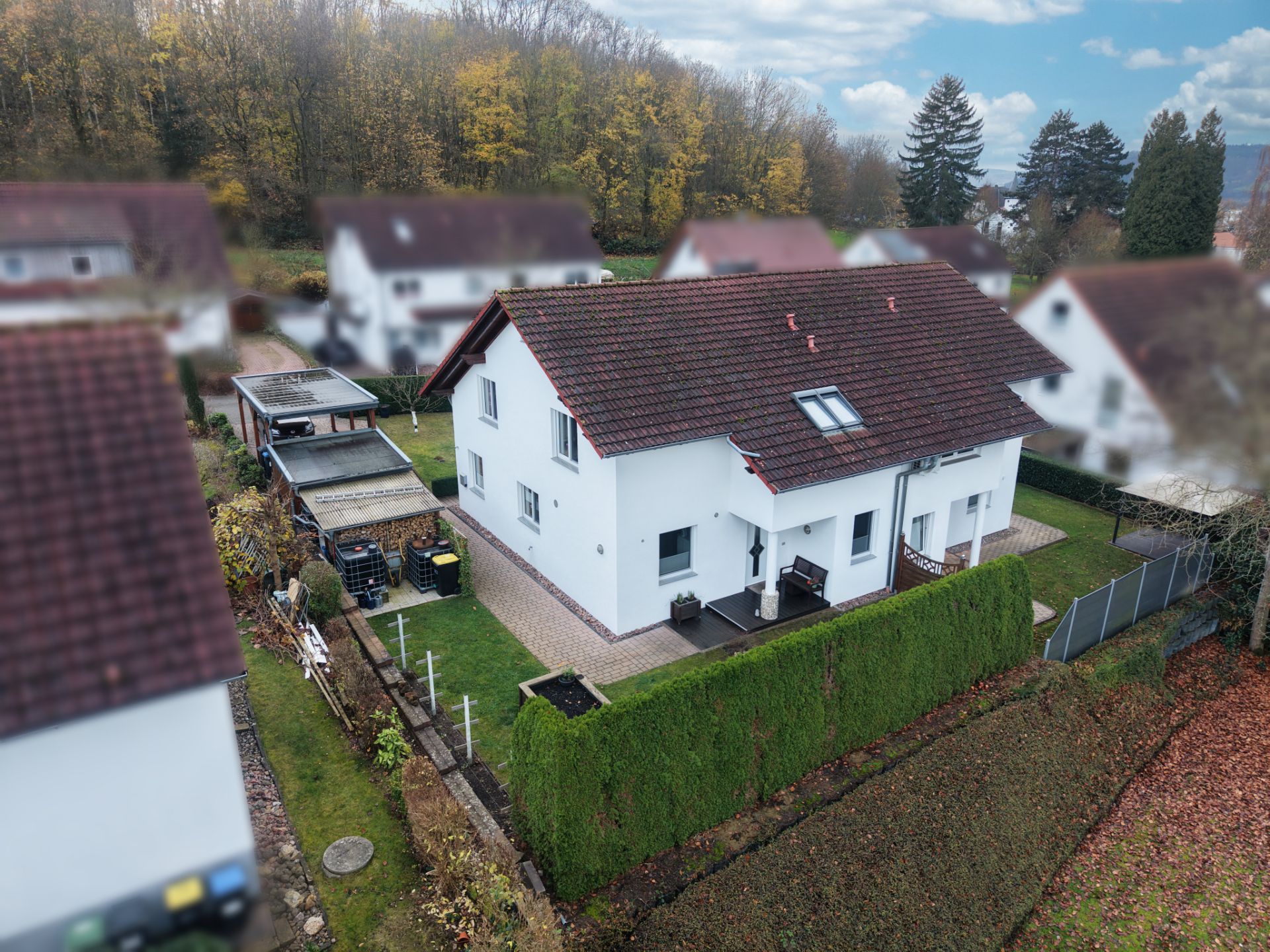 Luftaufnahme eines weißen Einfamilienhauses mit rotem Dach und gepflegtem Garten.
