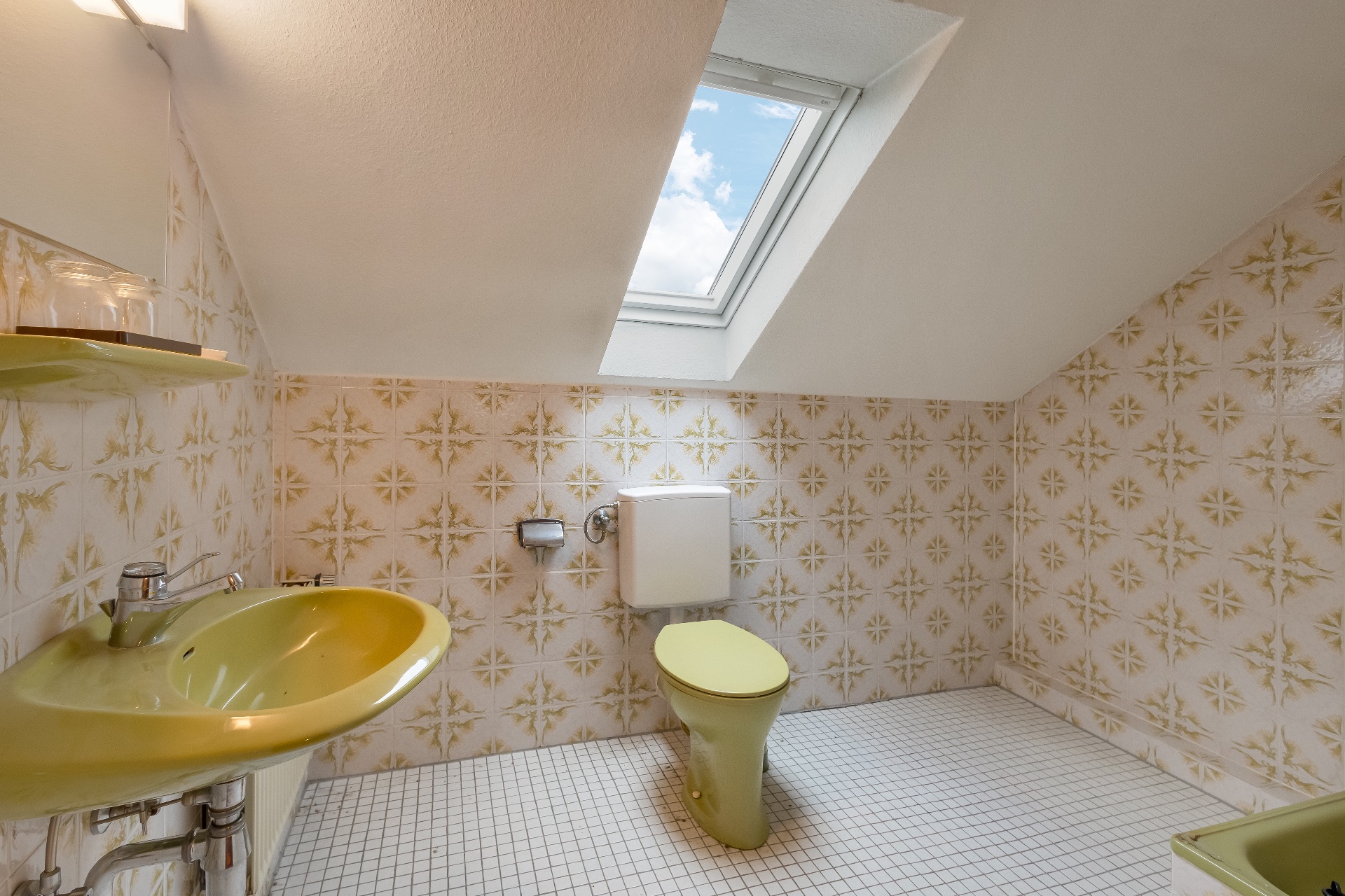Badezimmer mit grünem Waschbecken und Toilette, gemusterte Fliesen, Dachfenster.