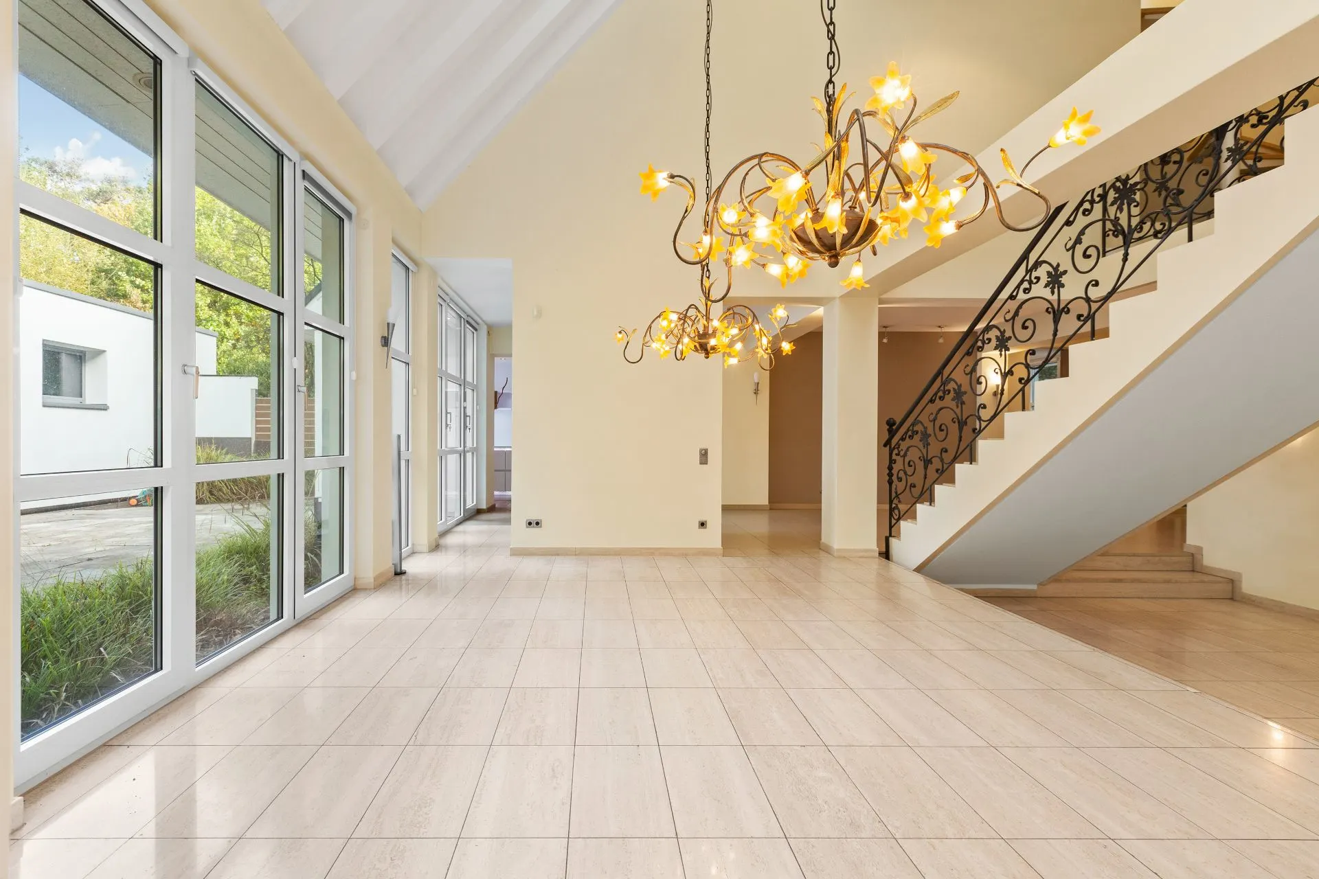 Heller Eingangsbereich mit großen Fenstern, Treppe und dekorativem Kronleuchter.