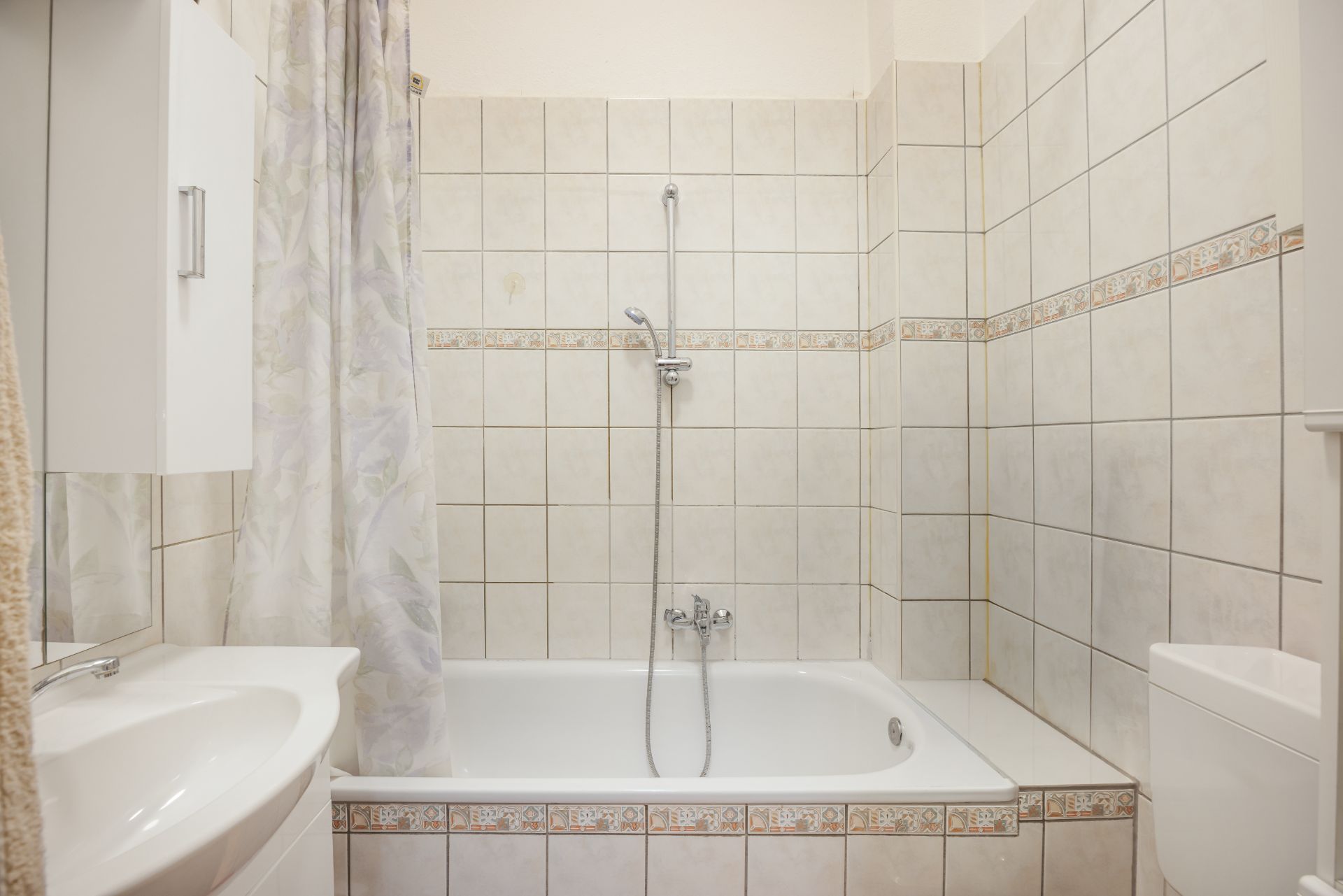 Helles Badezimmer mit Badewanne, Duschvorhang, weißen Fliesen und Waschbecken.