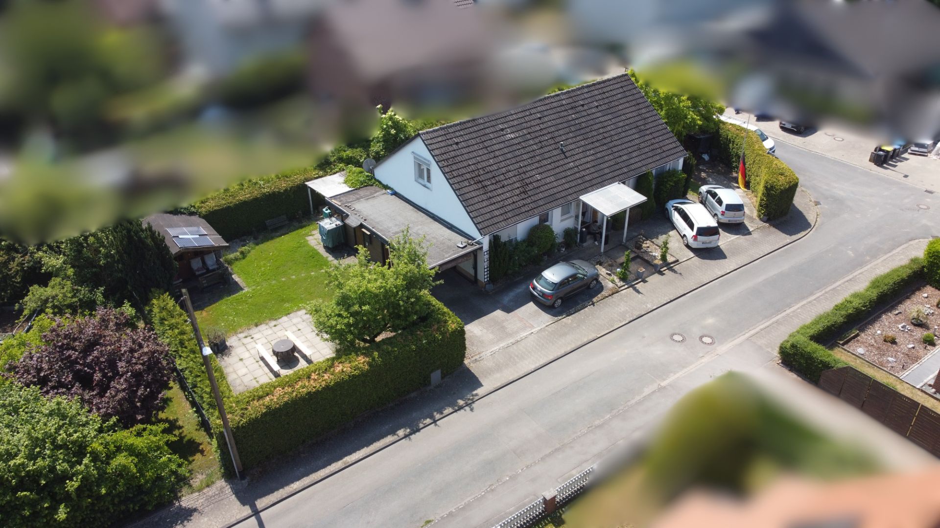 Luftaufnahme eines Einfamilienhauses mit Garten, Terrasse und zwei Autos in der Einfahrt.