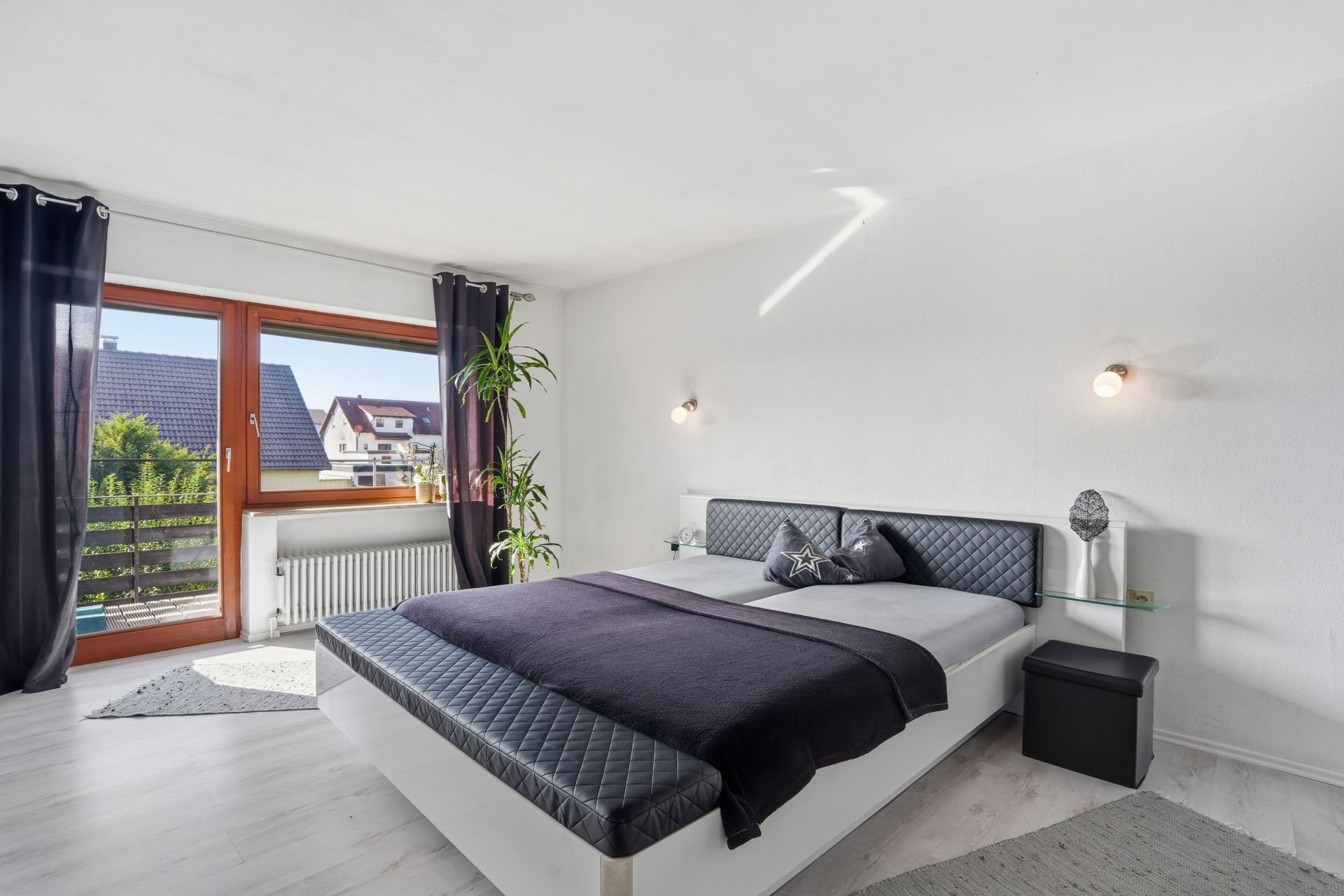 Helles Schlafzimmer mit Doppelbett, Pflanzen und großem Fenster mit Blick nach draußen.
