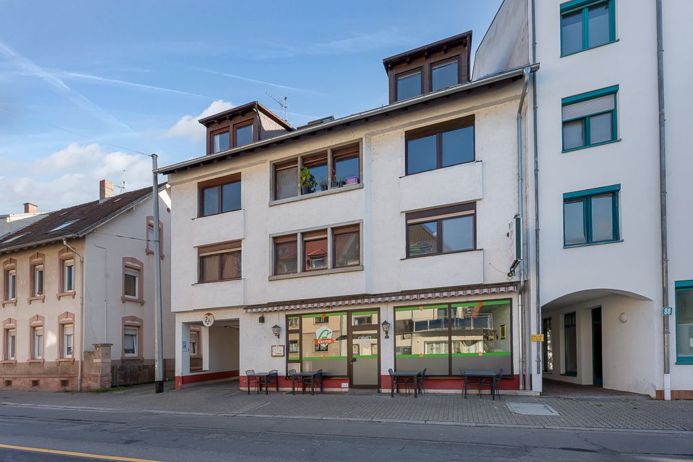 Dreistöckiges Wohnhaus mit großen Fenstern und Sitzgelegenheiten vor dem Eingang.