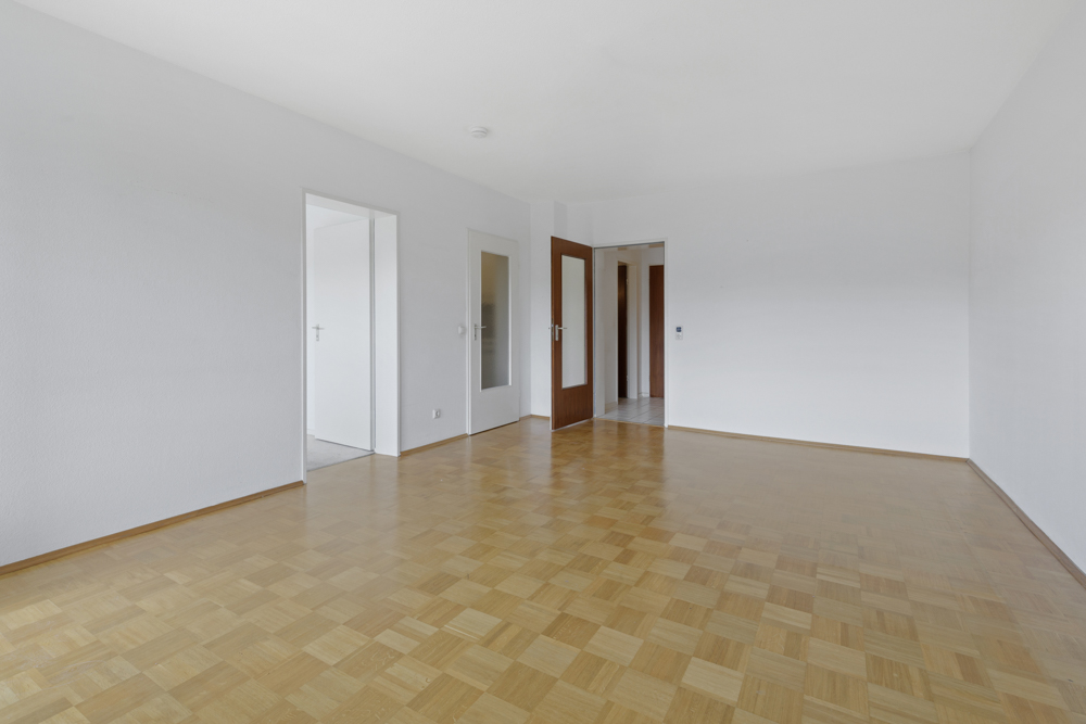 Leerer Raum mit Parkettboden und weißen Wänden, zwei Türen führen in andere Zimmer.