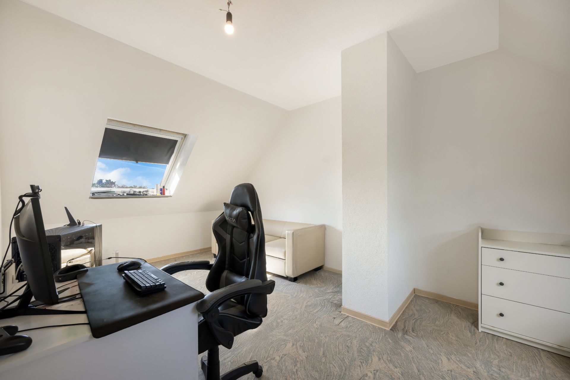 Helles Arbeitszimmer mit Schreibtisch, Bürostuhl, Sofa und Dachfenster.