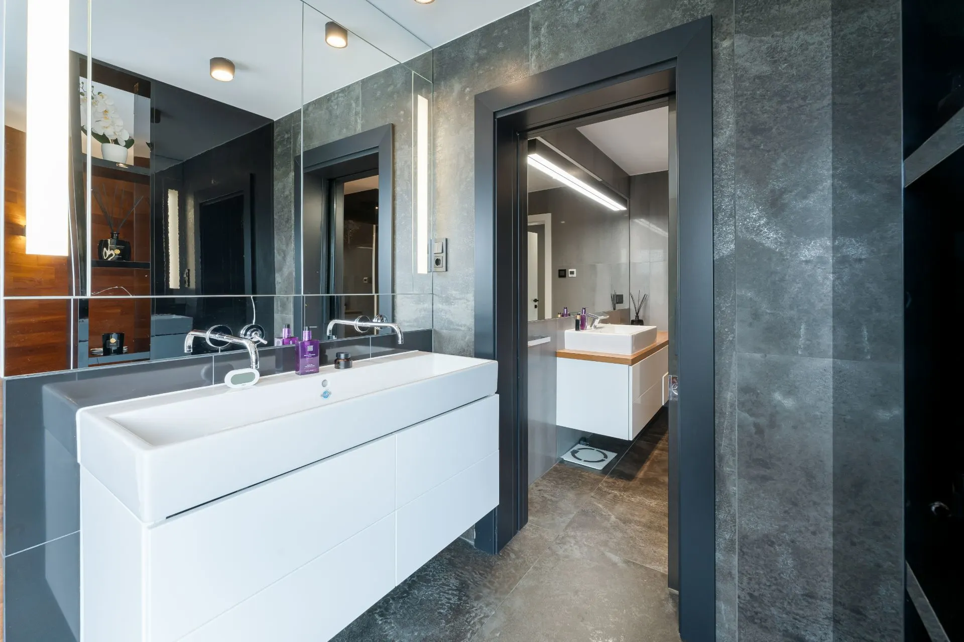Modernes Badezimmer mit großem Spiegel, weißen Waschbecken und grauen Wänden.