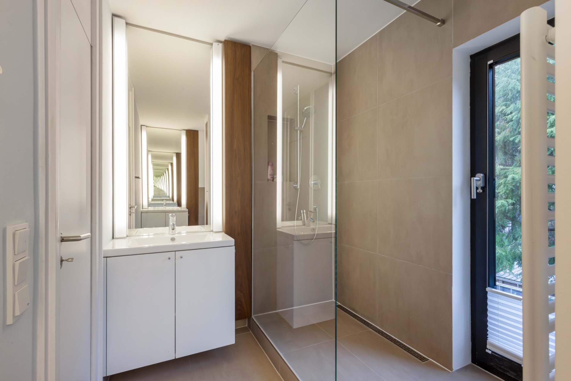 Modernes Badezimmer mit Dusche, großem Spiegel und Fenster mit Blick ins Grüne.