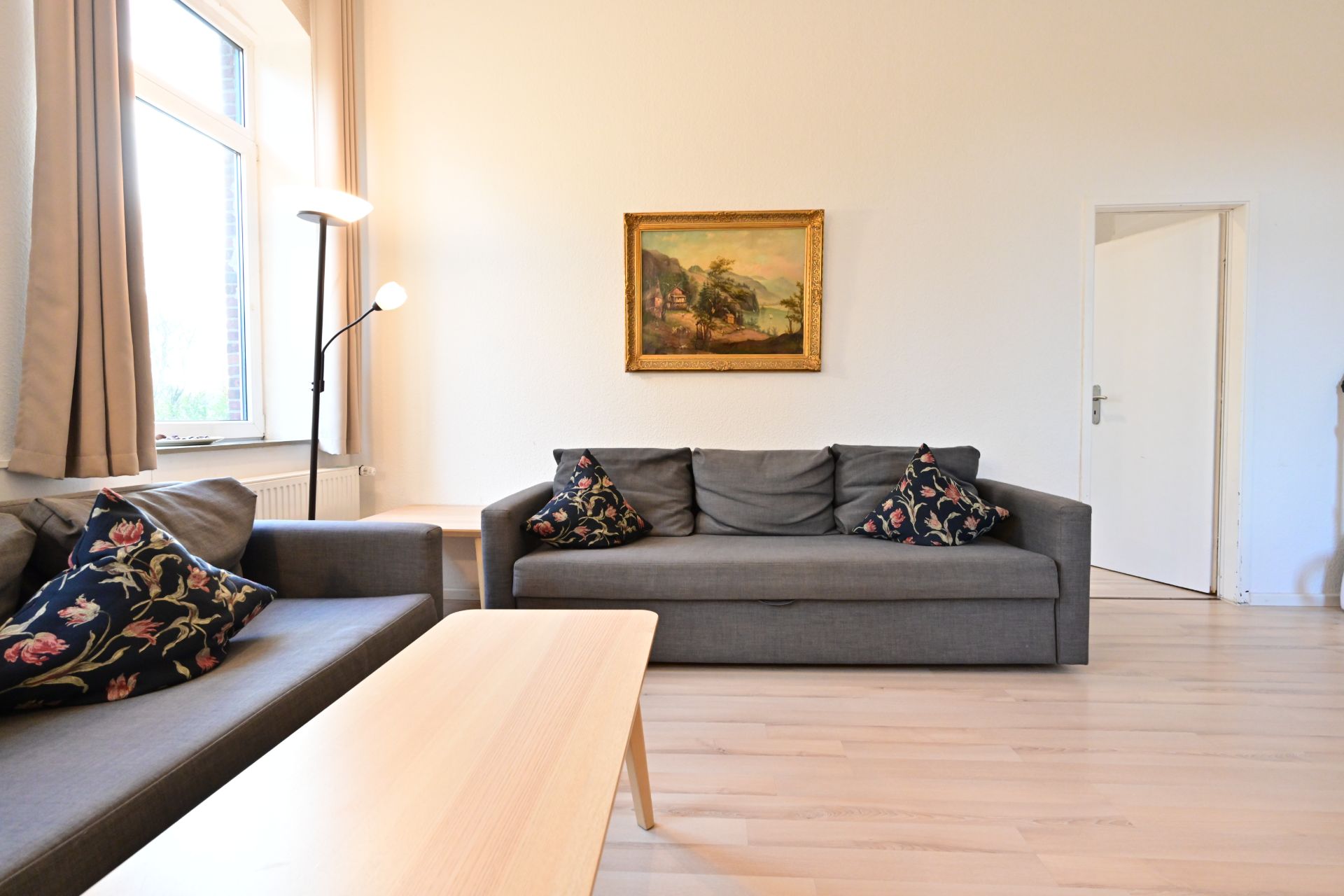 Wohnzimmer mit zwei grauen Sofas, Holztisch, Stehlampe und Bild an der Wand.