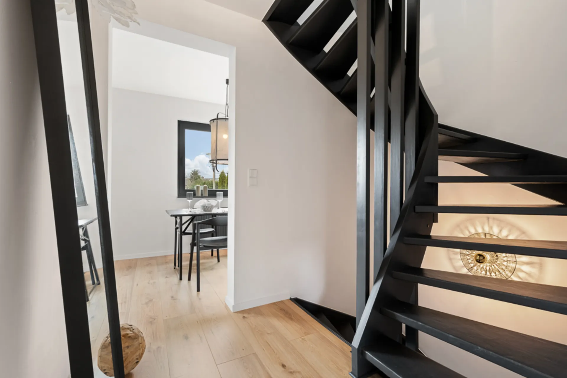 Flur mit schwarzer Treppe, großem Spiegel und Blick in ein Esszimmer mit Fenster.