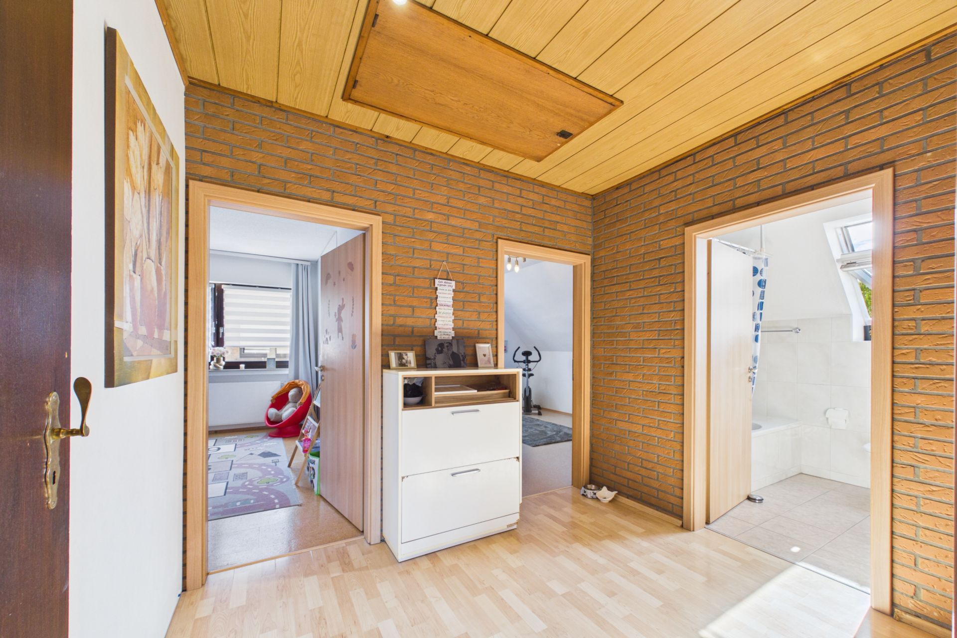 Heller Flur mit drei Türen zu verschiedenen Zimmern und einer Leiterluke in der Holzdecke.