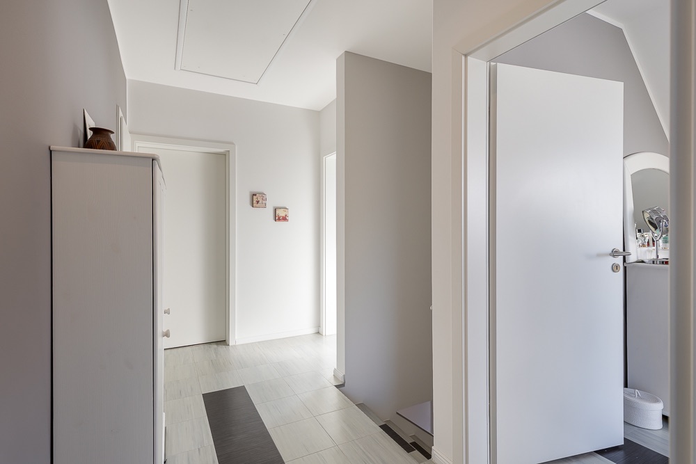 Heller Flur mit offener Tür, Kommode und Blick in ein weiteres Zimmer.