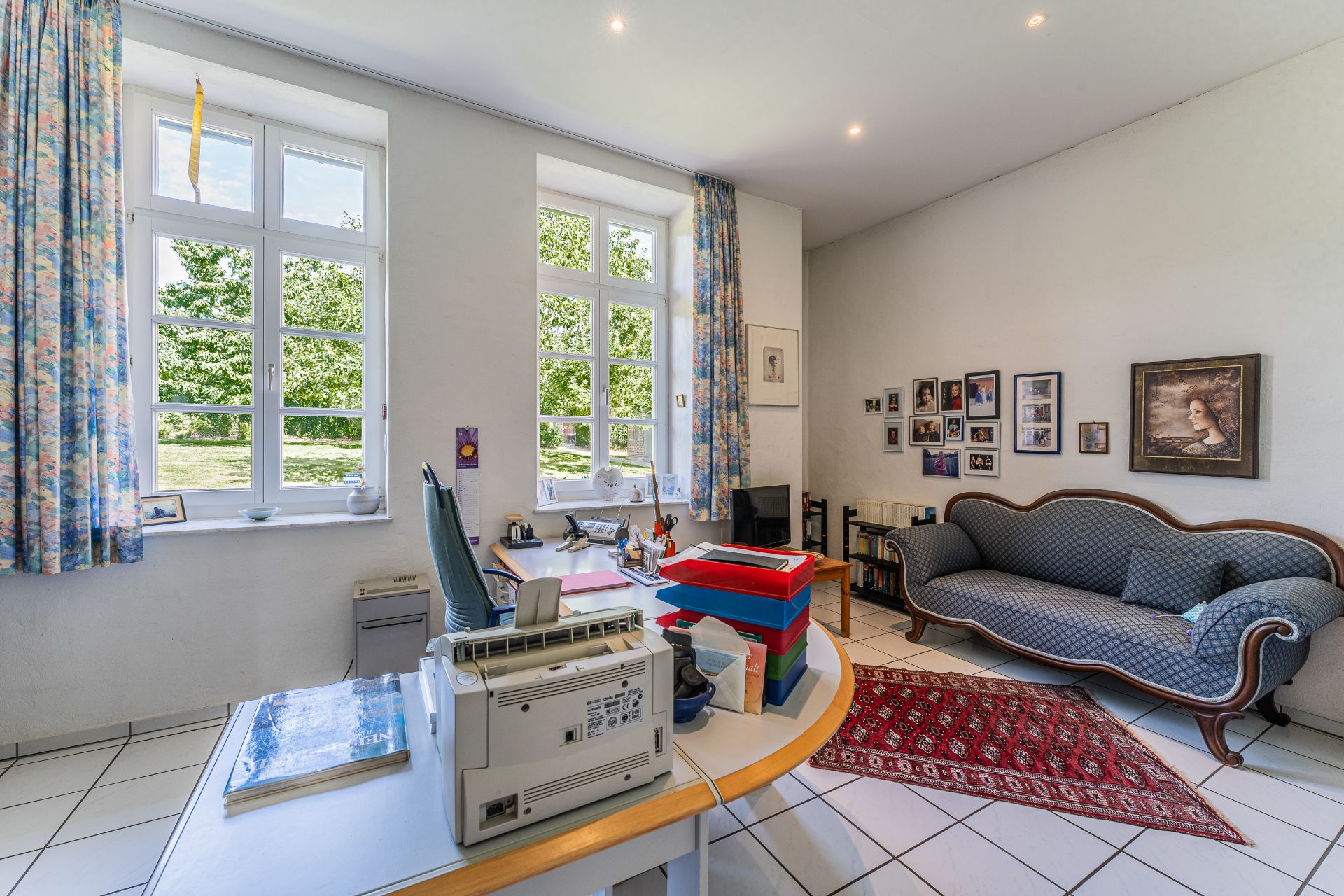 Helles Arbeitszimmer mit großem Schreibtisch, Sofa, Teppich und großen Fenstern.