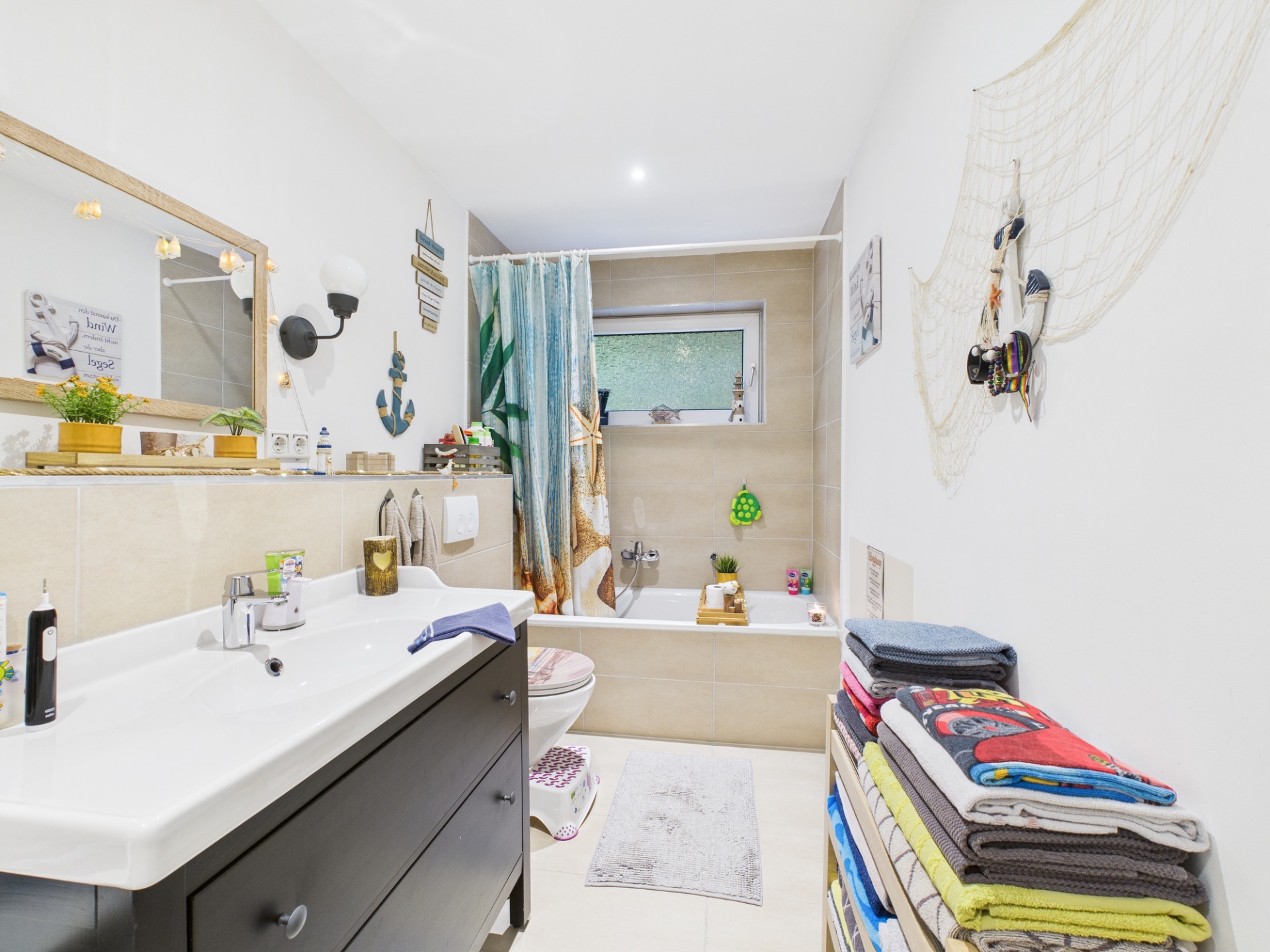 Helles Badezimmer mit Waschbecken, Badewanne, Spiegel und einem Regal mit bunten Handtüchern.