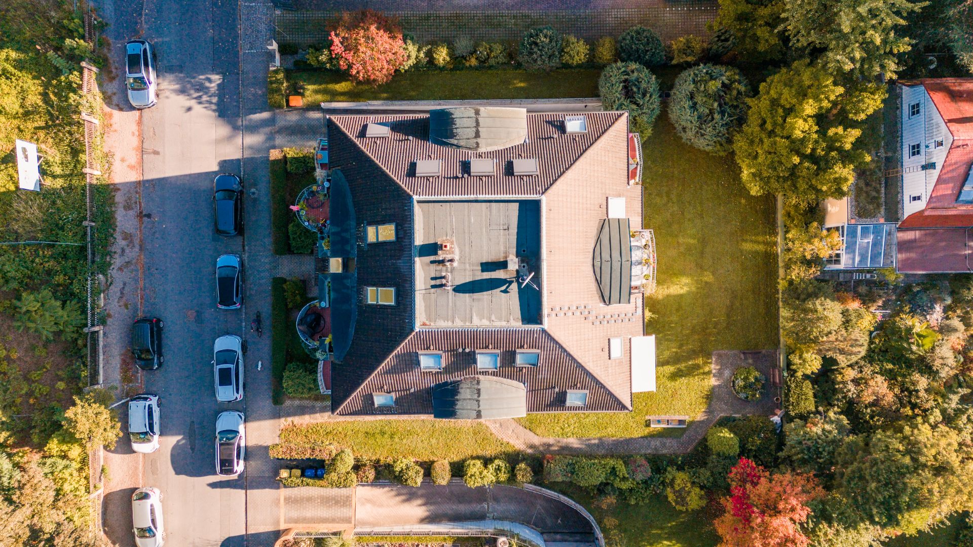 Luftaufnahme eines Hauses mit Garten und geparkten Autos auf der Straße.