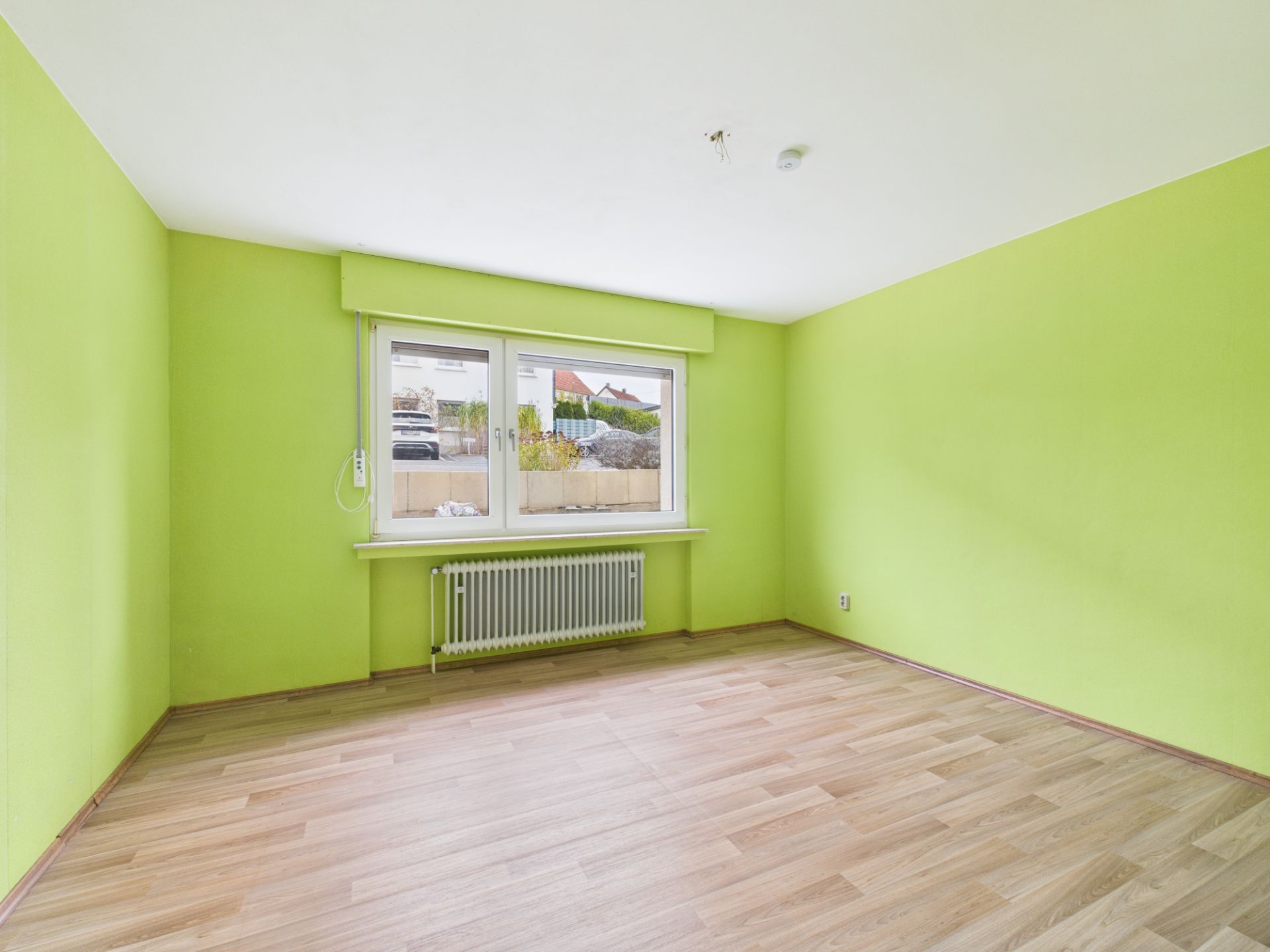 Leerer Raum mit grünen Wänden, großem Fenster und hellem Holzboden.
