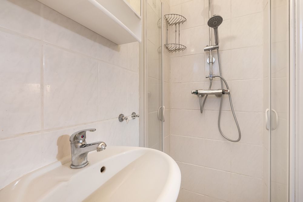 Nahaufnahme von Waschbecken und Duschkabine mit Armaturen in einem gefliesten Badezimmer.