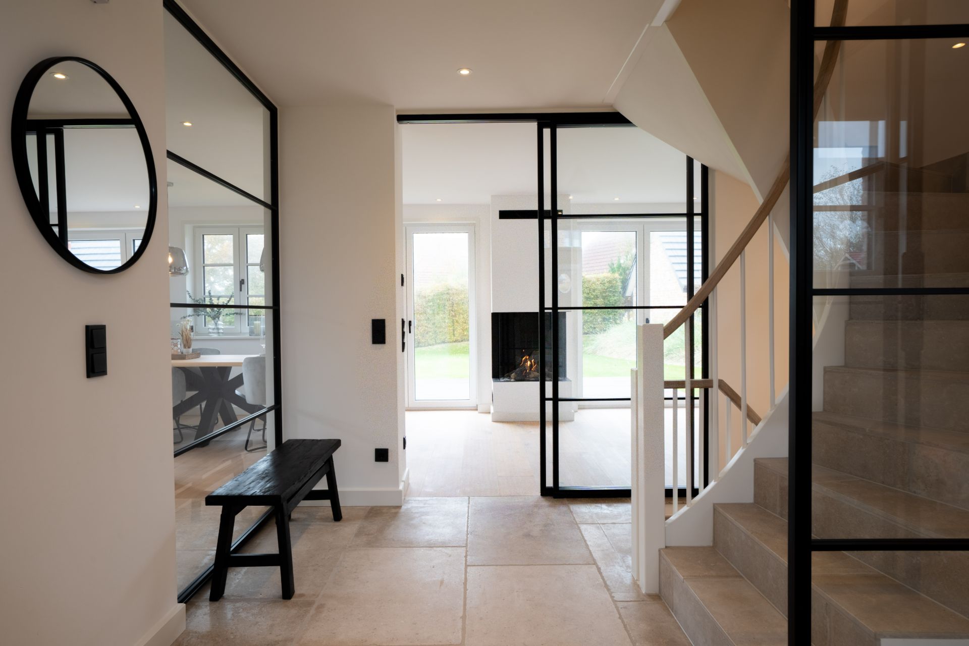 Eingangsbereich mit Treppe, Bank, rundem Spiegel und Blick auf Wohnzimmer mit Kamin.