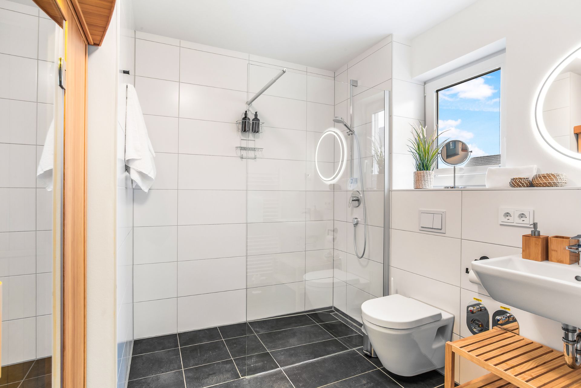 Helles Badezimmer mit begehbarer Dusche, WC, Waschbecken und Fenster.