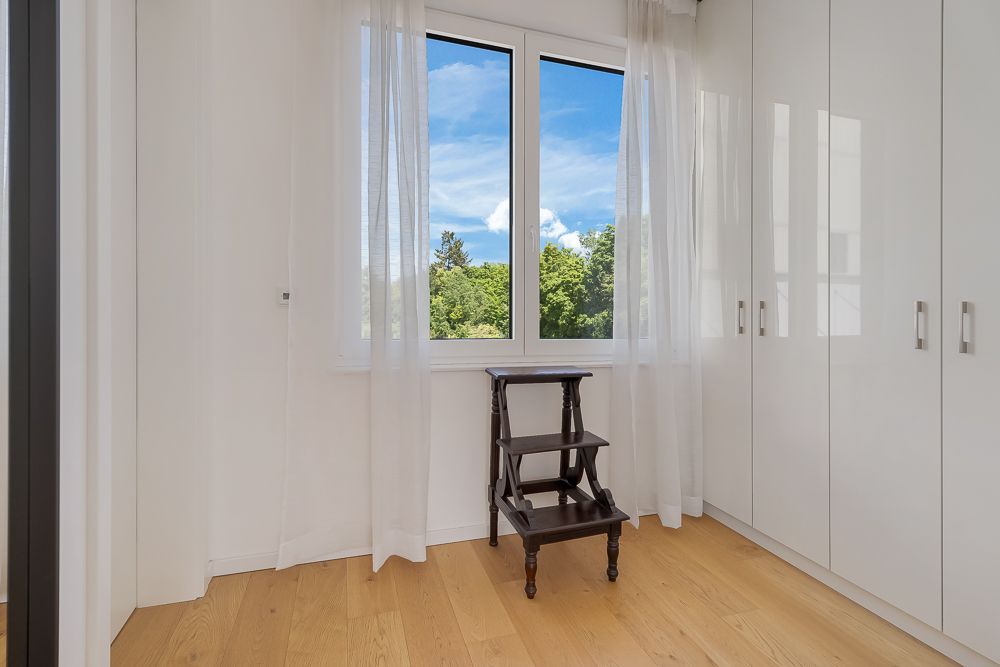 Heller Raum mit weißen Einbauschränken, Holzfußboden und Fenster mit Blick ins Grüne.