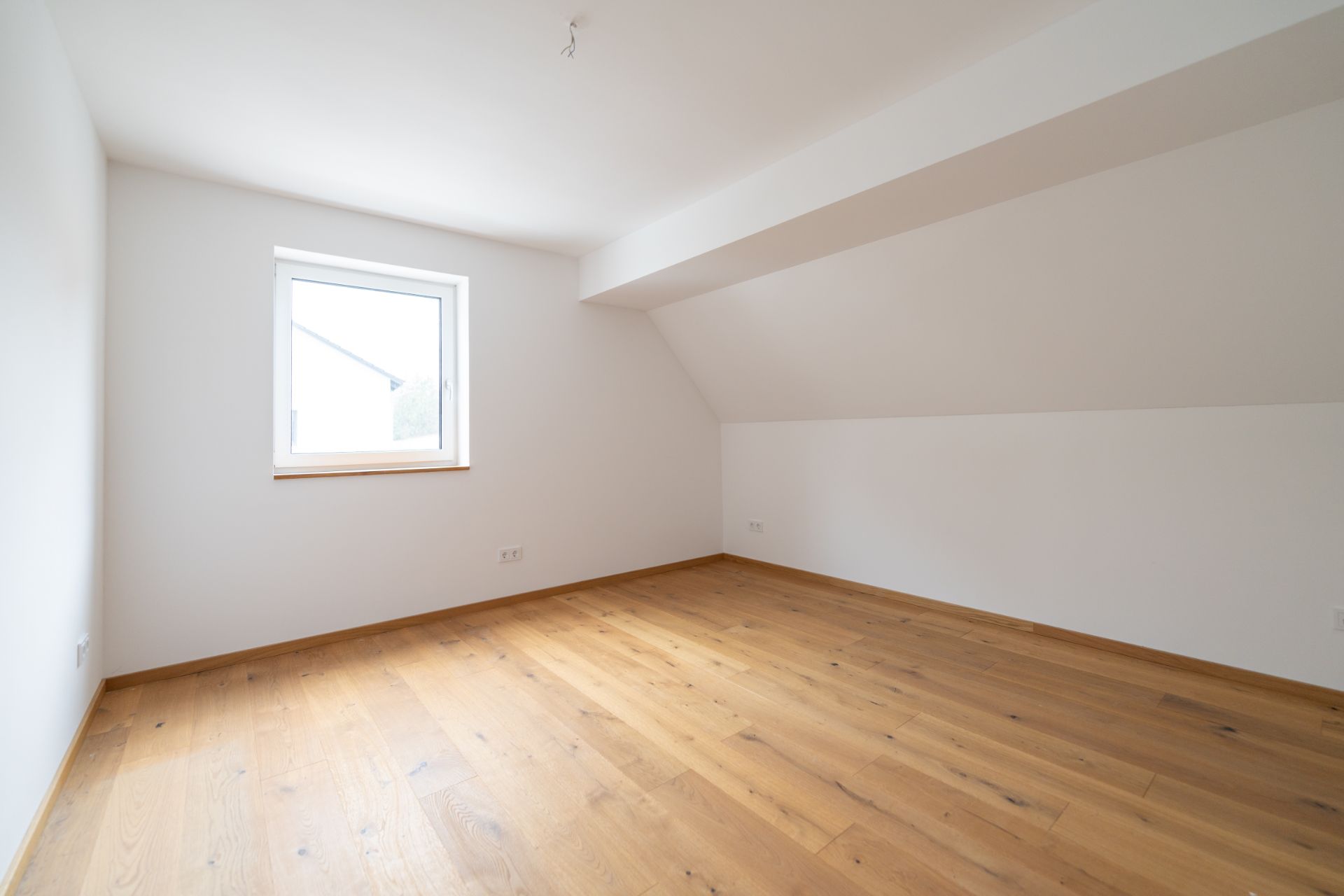 Leerer Raum mit weißer Wand, Holzfußboden und einem Fenster.