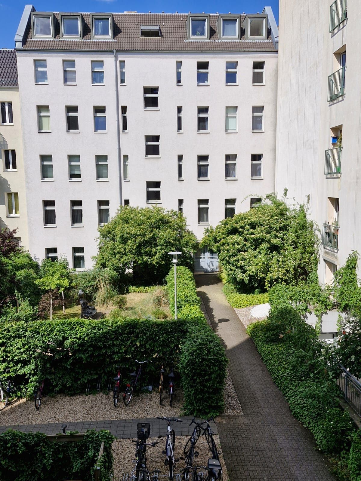 Innenhof mit Grünflächen, Fahrrädern und Mehrfamilienhaus im Hintergrund bei sonnigem Wetter.