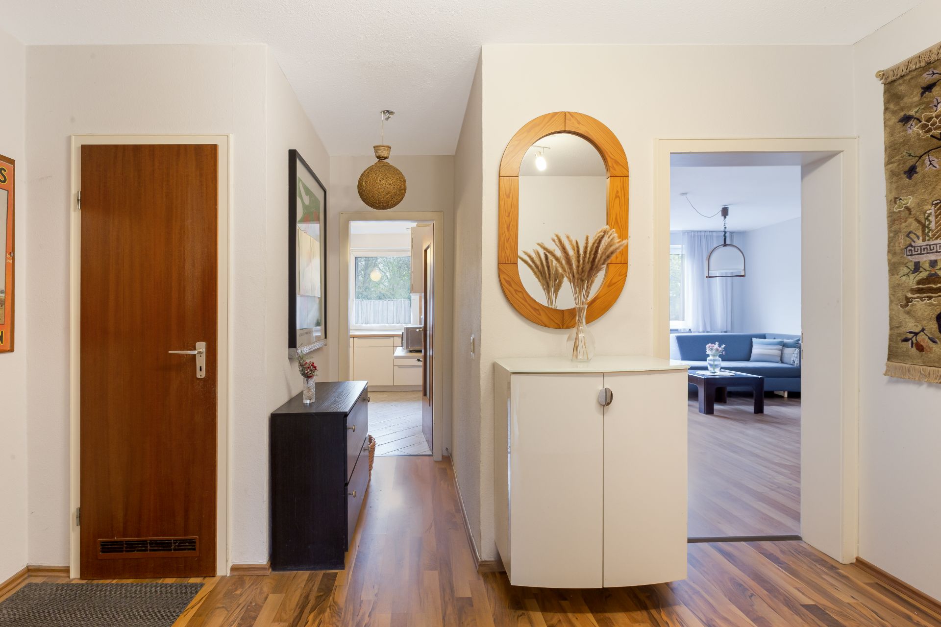 Hausflur mit Holzfußboden, Kommode mit Spiegel, Blick ins Wohnzimmer und weiteres Zimmer.