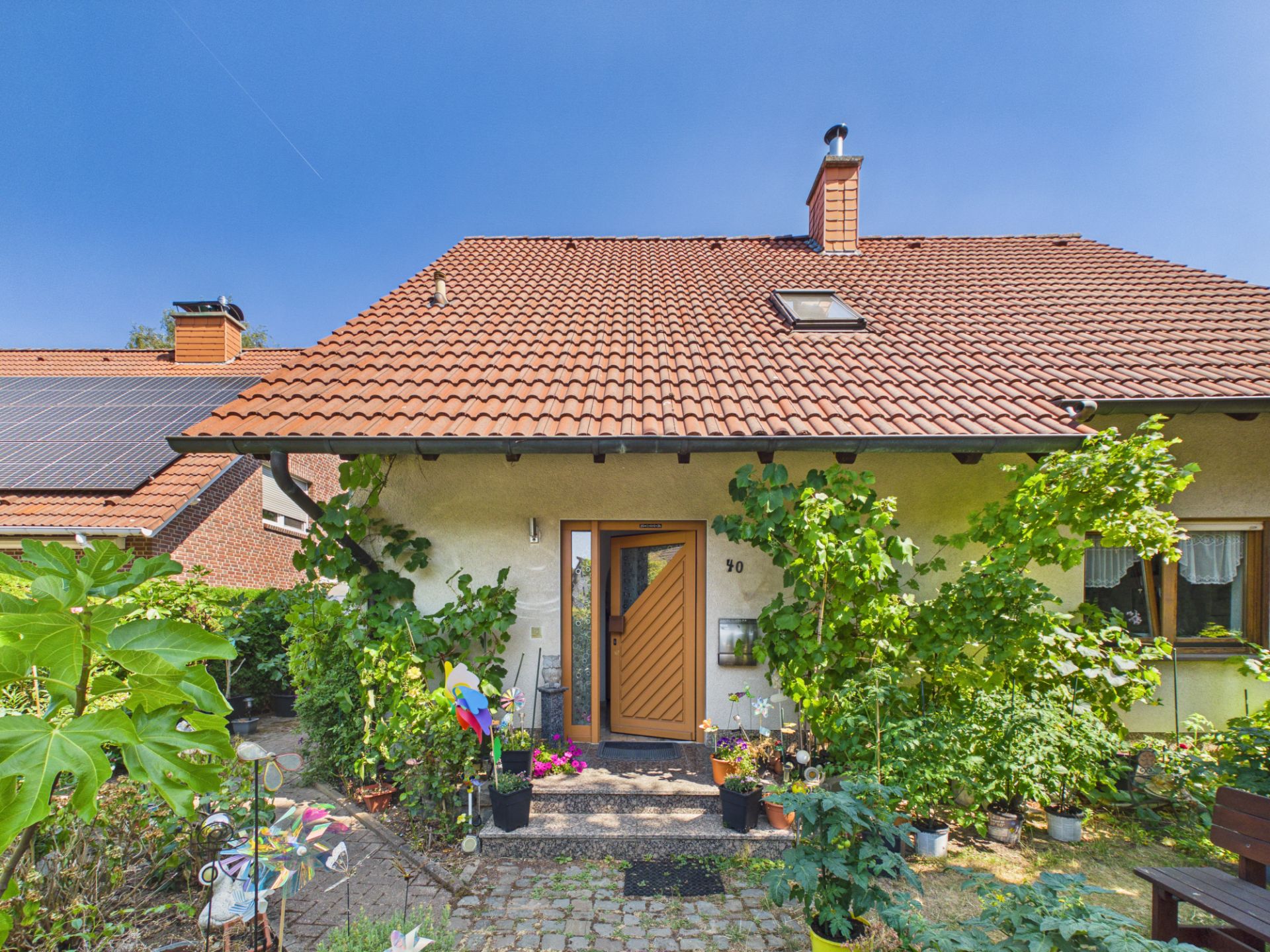 Einfamilienhaus mit rotem Ziegeldach, Garten und Pflanzen vor dem Eingang.