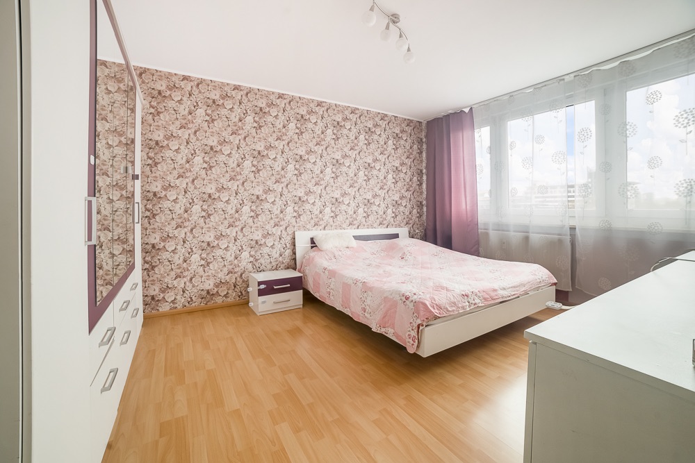 Helles Schlafzimmer mit Blumenmuster-Tapete, Doppelbett, Kleiderschrank und großen Fenstern.