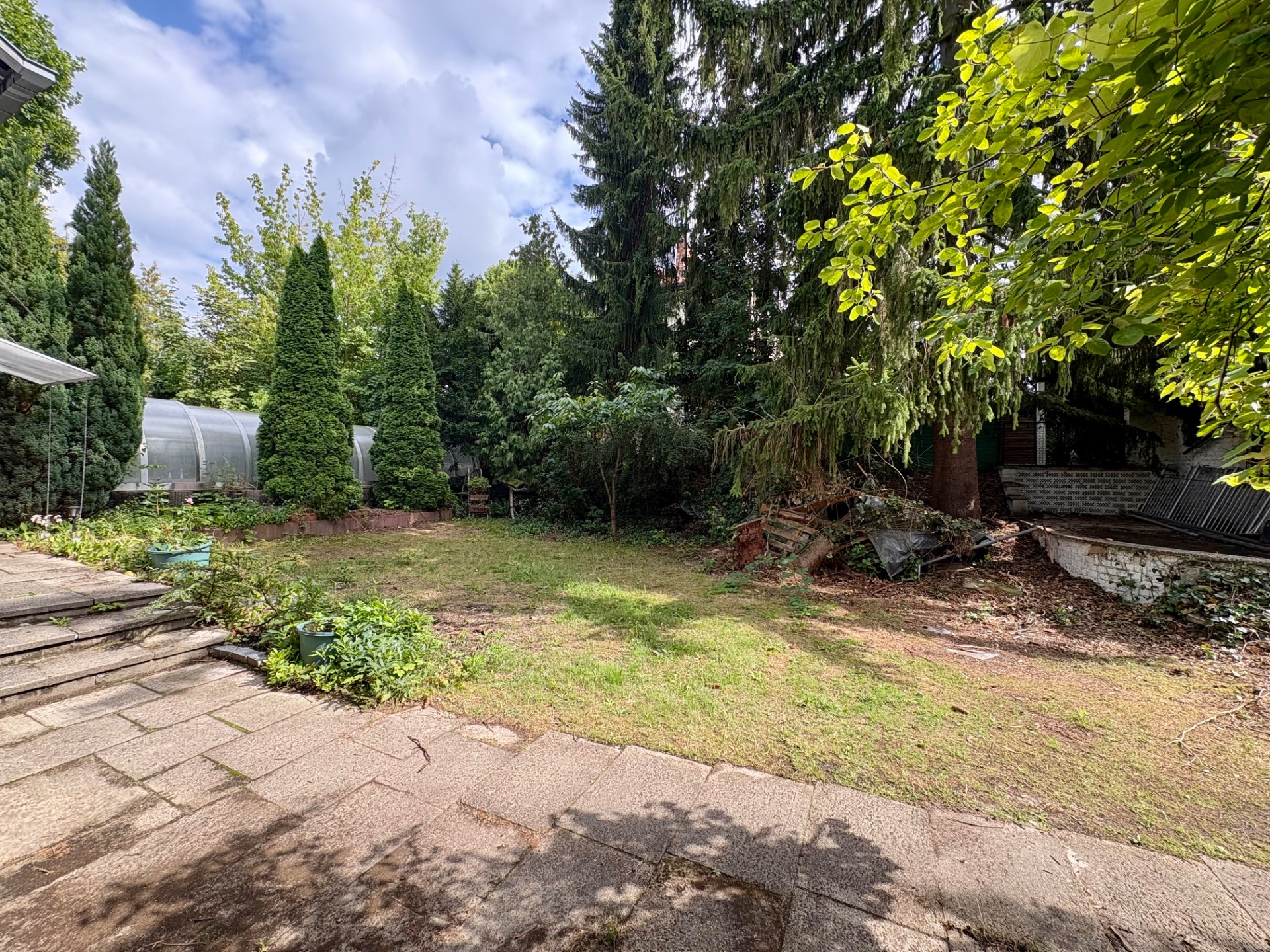 Garten mit Rasenfläche, Bäumen und einer gepflasterten Terrasse im Vordergrund.