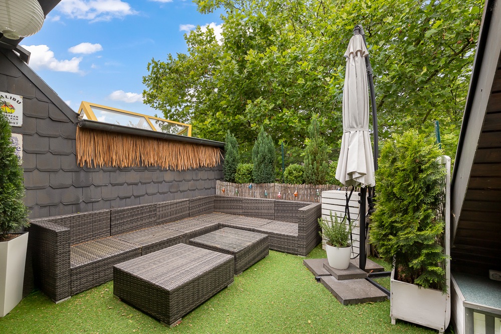 Gemütliche Dachterrasse mit Rattan-Sitzgruppe, Sonnenschirm und viel Grün.