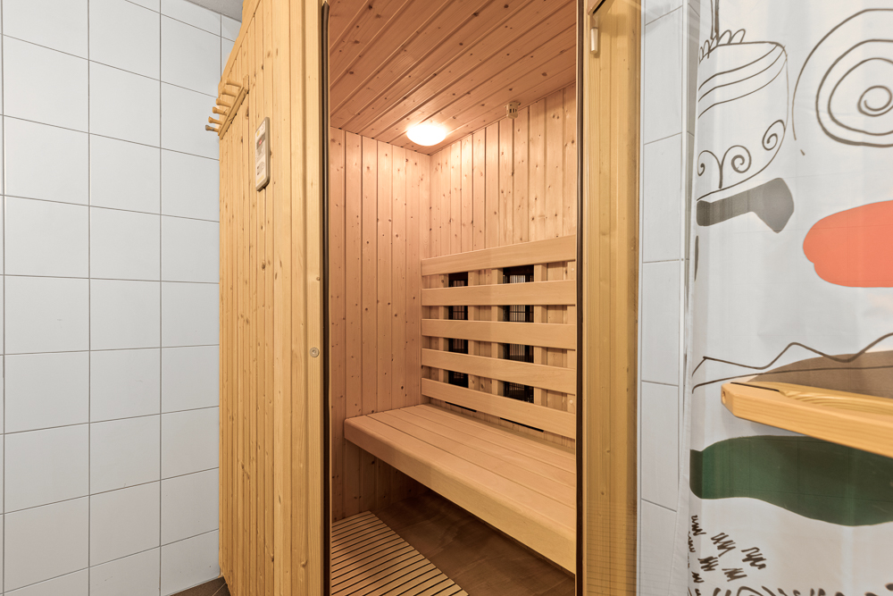 Holzsauna mit Bank in einem gefliesten Raum und sichtbarem Duschvorhang.