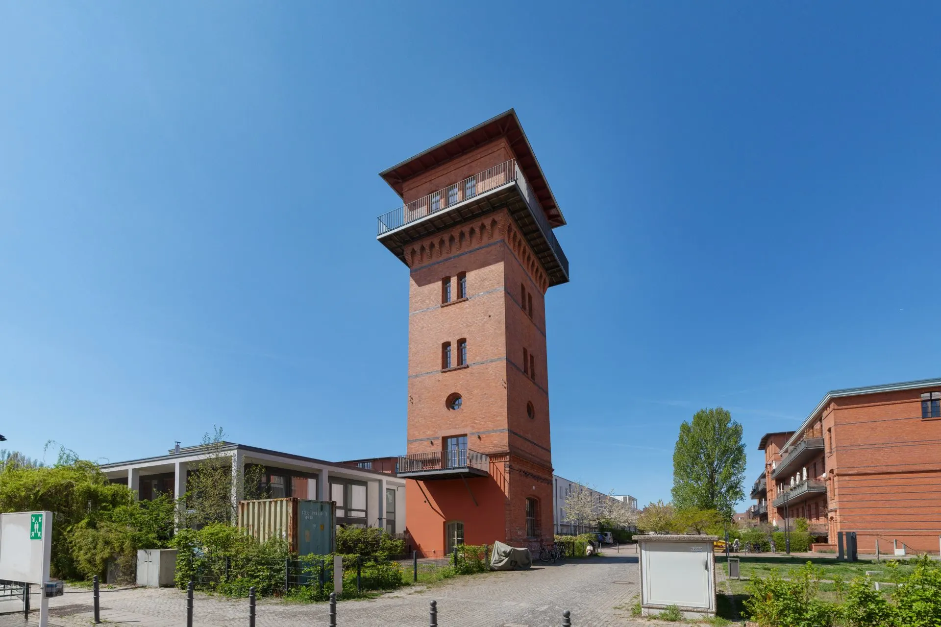Backsteinturm mit Flachdach in Wohnanlage, umgeben von modernen Gebäuden und Grünflächen.