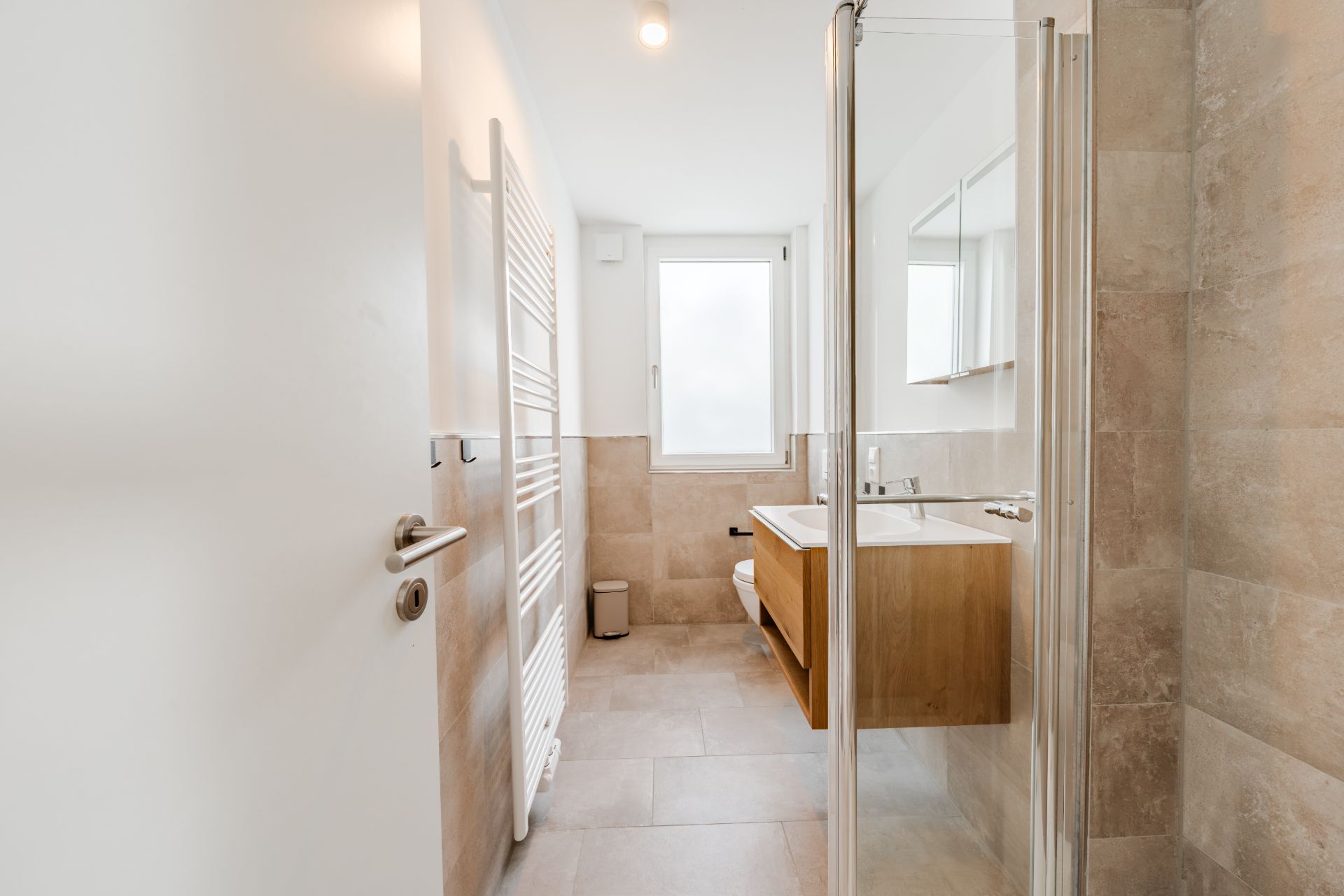 Helles Badezimmer mit Dusche, Waschbecken, Spiegel und Fenster.