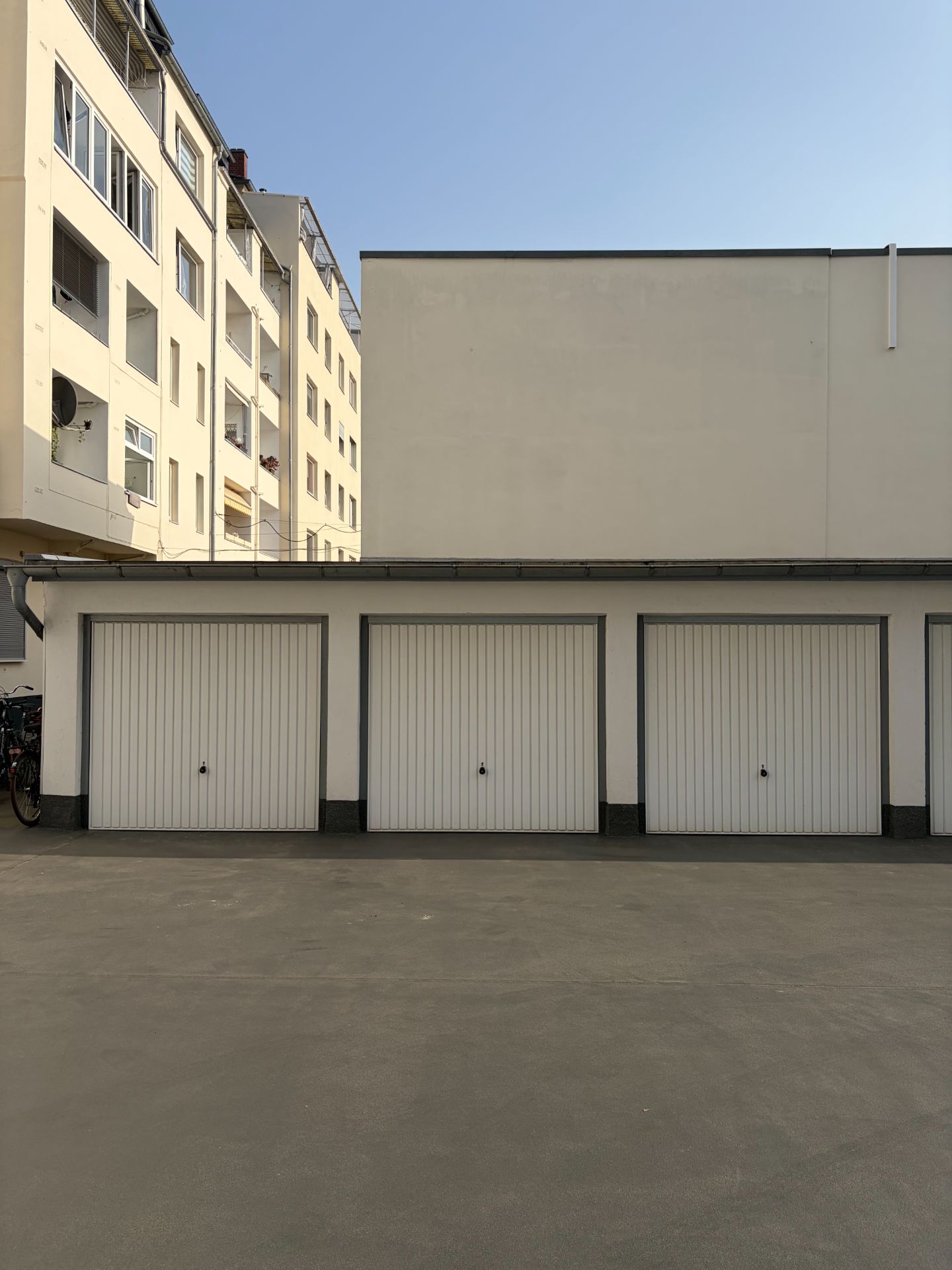 Drei geschlossene Garagentore vor einem Wohngebäude, daneben Fahrräder.